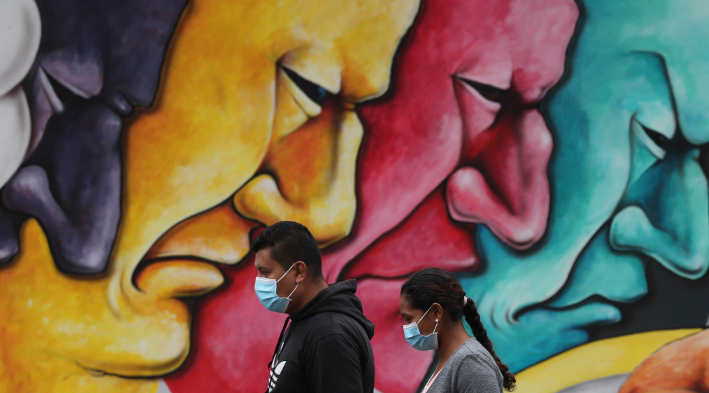 Pedestrians, wearing protective face masks as a precaution against the spread of the new coronavirus, walk past a mural in Quito, Ecuador, Saturday, March 28, 2020. The government has declared a health emergency, enacting a curfew and restricting movement to only those who provide basic services. (AP Photo/Dolores Ochoa)